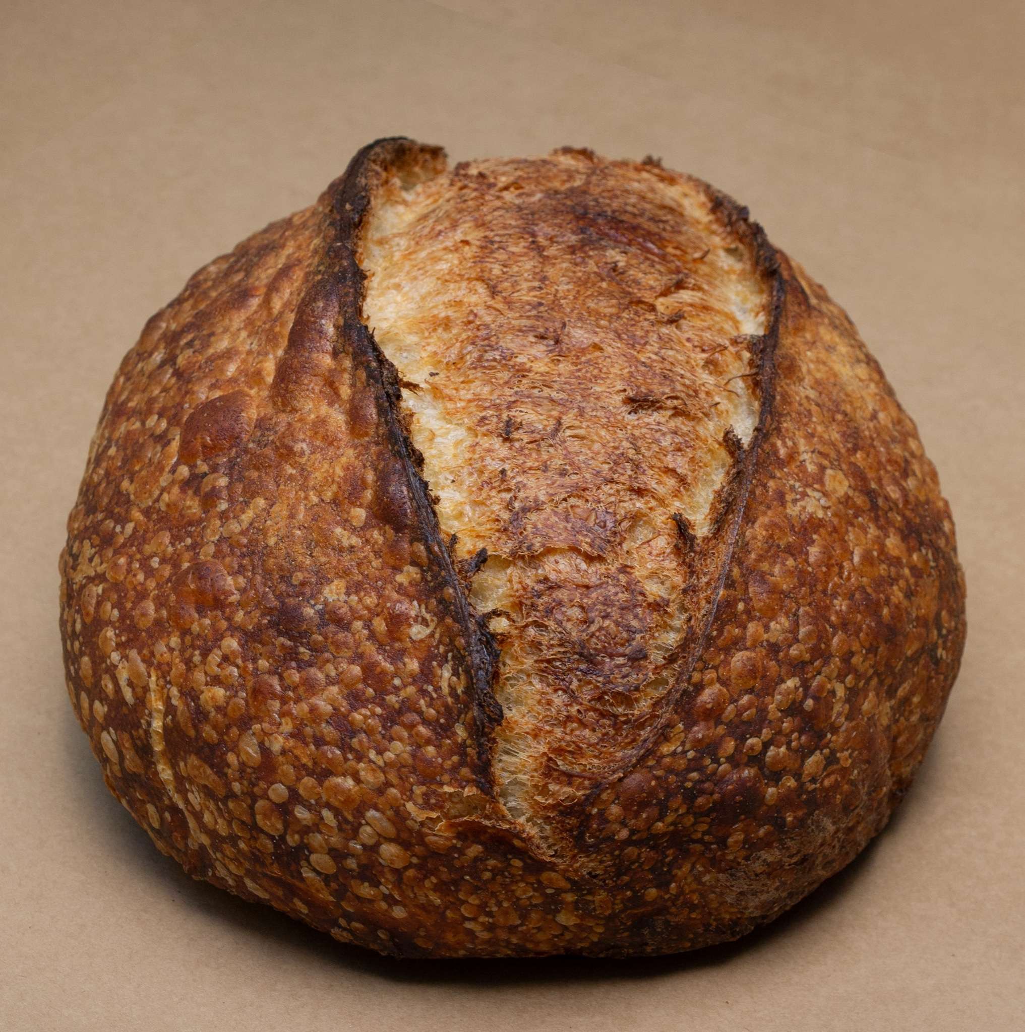 A Billy Bread rustic sourdough loaf with a blistered golden crust and a single dramatic score, on brown kraft paper.