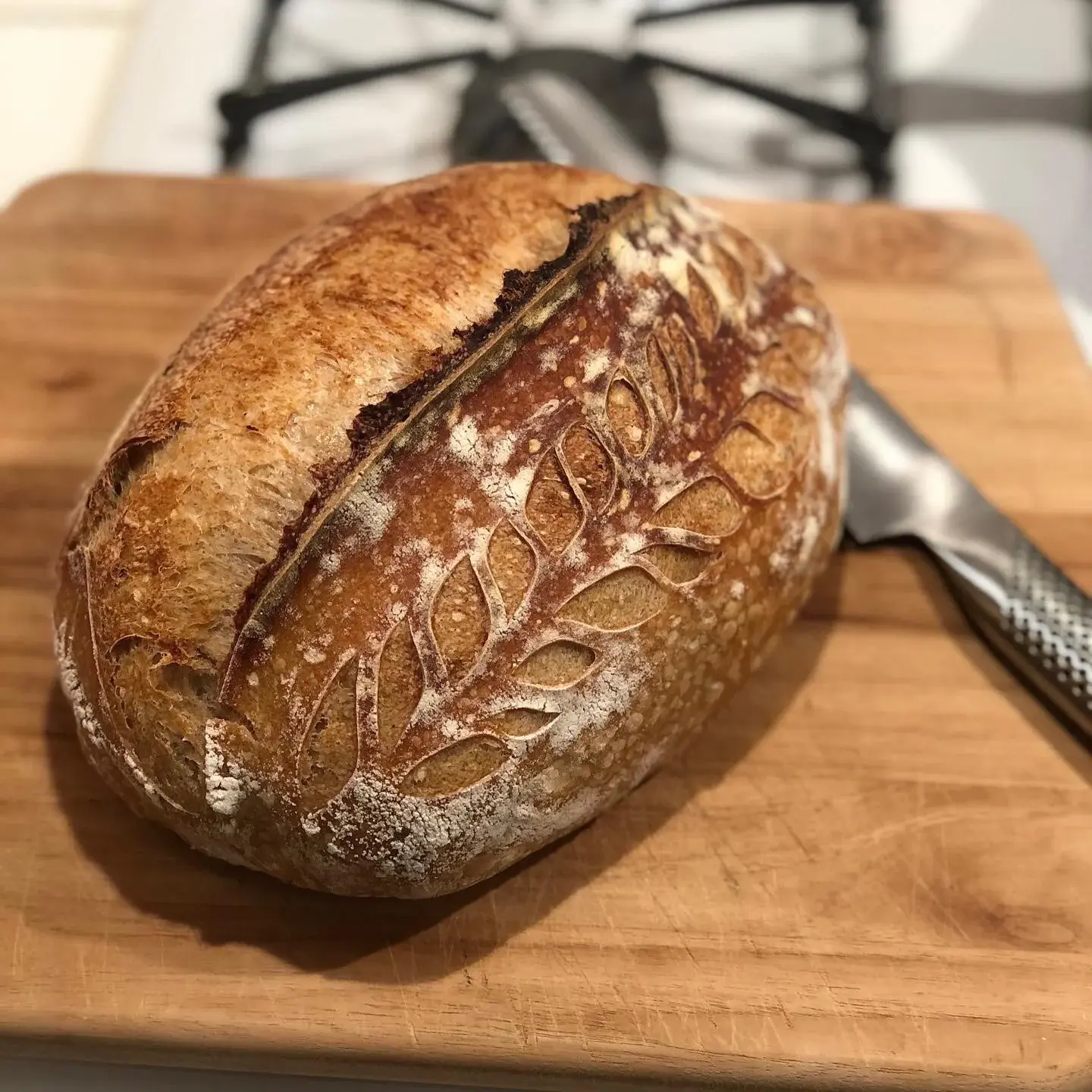 A Billy Bread sourdough boule scored with a wheat-stalk pattern, resting on a wooden board.