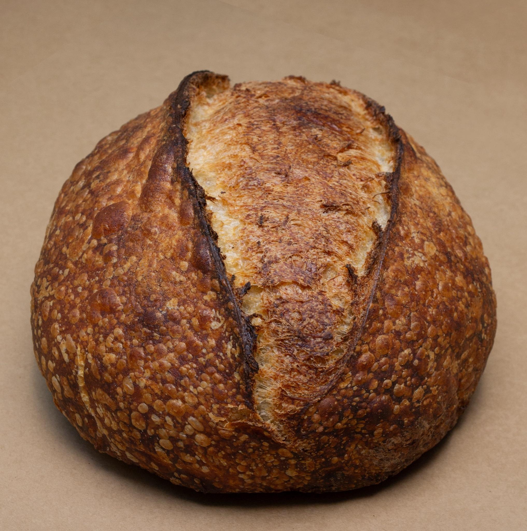 A Billy Bread rustic sourdough loaf with a blistered golden crust and a single dramatic score, on brown kraft paper.